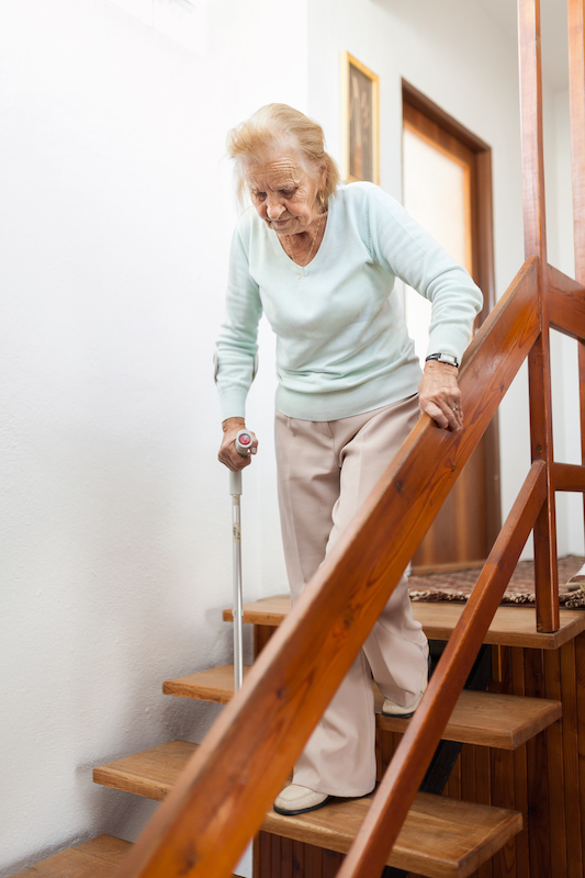 Elderly woman at home using a walking cane to get down the stairs